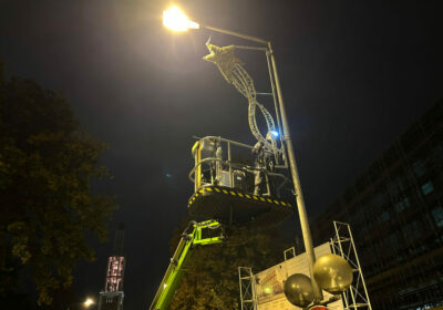 Ein Arbeiter montieren in den dunklen Morgenstunden als Teil der Winterbeleuchtung ein winterliches Lichtelement in Sternform an einer Straßenlaterne in Wolfsburg.
